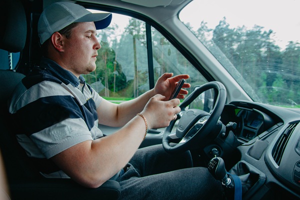 A truck driver looking down at a smartphone while behind the wheel, illustrating the dangerous distracted driving behaviors that lead to serious commercial vehicle accidents in Palm Beach Gardens, Florida.