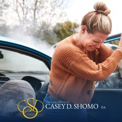 After a car accident in Palm Beach Gardens, a passenger grimaces while holding her neck, a sign of whiplash